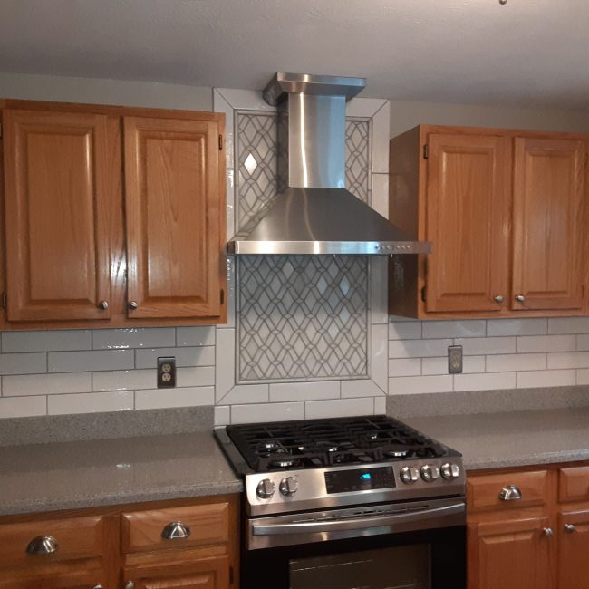 White Subway Tile with Marble Focal Inlay Large white subway tile backsplash with a central marble inlay feature in a bright kitchen