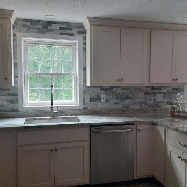 Gray Stacked Stone Tile Backsplash Gray stacked stone ceiling-high tile backsplash in a kitchen with white cabinets and stainless steel appliances